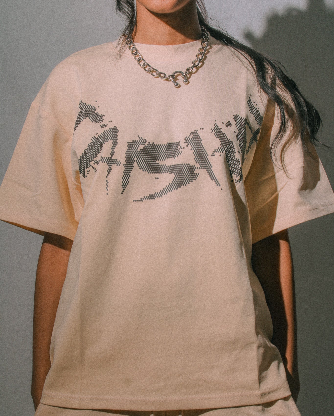 Person wearing a beige t-shirt with black text and matching pants against a neutral background