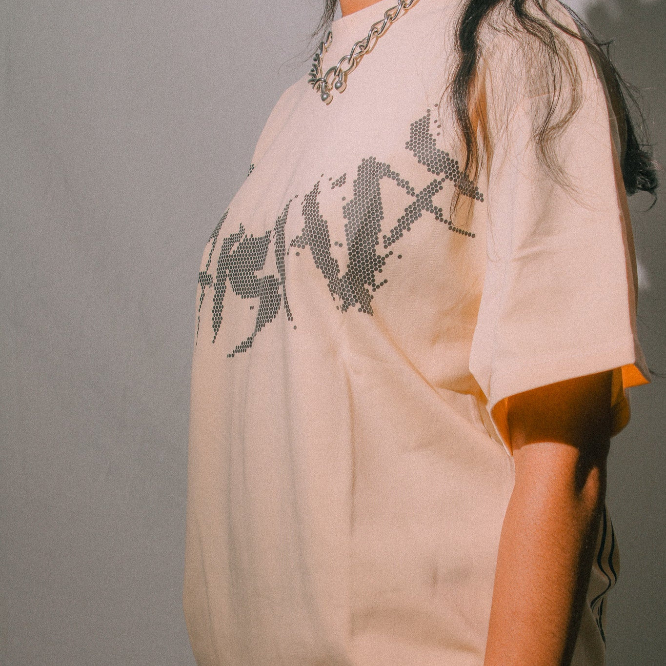 Person wearing a beige t-shirt with black graphic design against a plain background