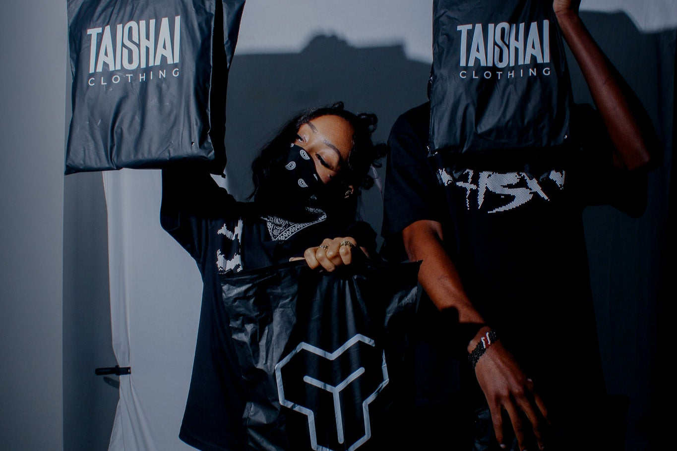 Person wearing a black outfit with 'Taishai Clothing' branding, standing against a dark background.