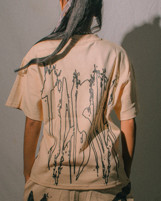 Person wearing a beige t-shirt and shorts set with black abstract designs, standing against a plain background.